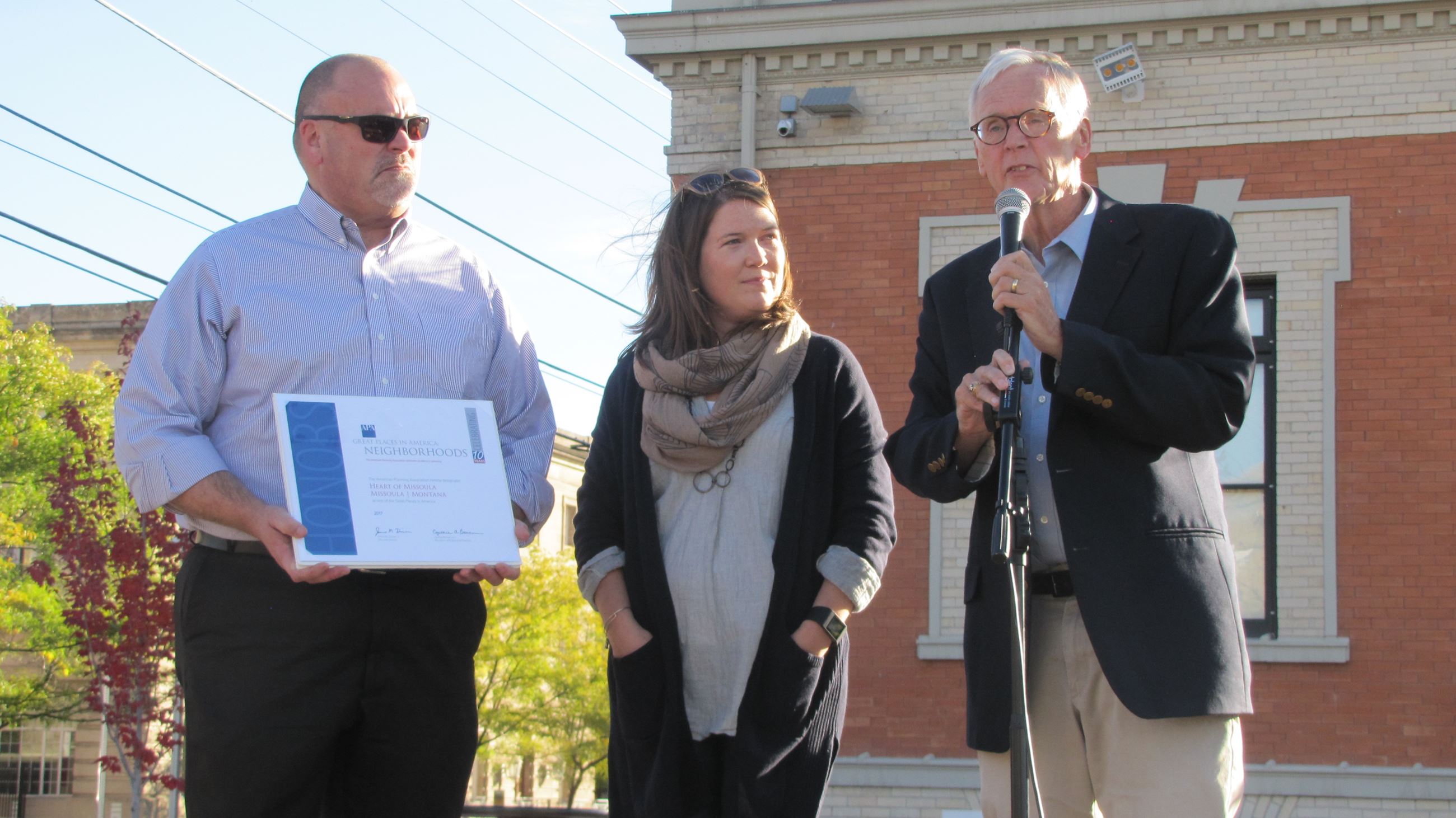 Mayor Engen, Allison Mouch, Dan Cederberg standing on stage as crowd gathers around